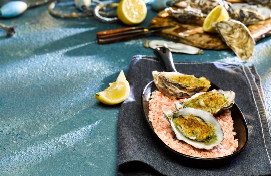 Food photograph close up of oysters rockefeller, baked oysters topped with breadcrumb and cheese mix, served in a cast iron pan filled with rock salt