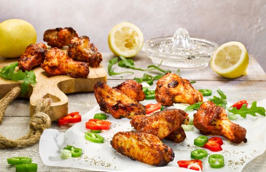 Food photograph close up of baked piri piri chicken wings served on a wooden board alongside lime wedges, coleslaw and thyme sprigs