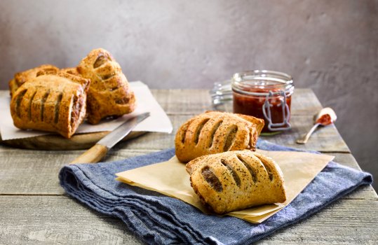 Food photograph close up of two artisan sausage rolls shot on brown paper with chilli chutney