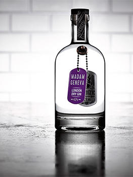 Drinks photograph of four bottles of small batch gin, each shown individually on a reflective metal tabletop with white subway tiles in the background