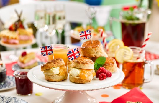 Food photograph of homemade lemon and raspberry scones, filled with lemon curd and clotted cream; served on a white ceramic cake stand on a Jubilee street party table