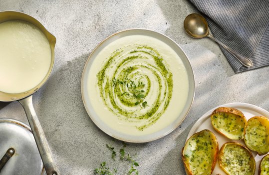 Aerial food photograph of a zero waste potato soup, silky potato soup served alongside crispy potato skins with cheese and garlic, with dill oil swirled into the top of the bowl of soup