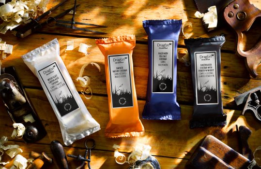 Aerial food photograph of four packs of Dragon Handcrafted cheddar cheese, surrounded on a wooden tabletop by vintage woodworking tools and wood shavings