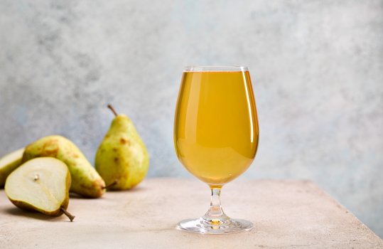 Drinks photograph of a glass of PGI traditional Welsh perry, shot on a textured grey and teal background with fresh green pears in the background