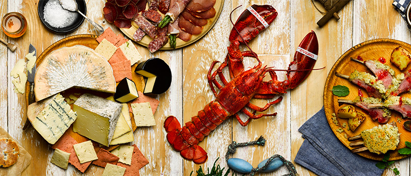 Aerial panoramic food photograph of a wide selection of Welsh produce, including cakes and patisserie, cheese, lobster, meat and poultry, pies, baked goods, and world foods