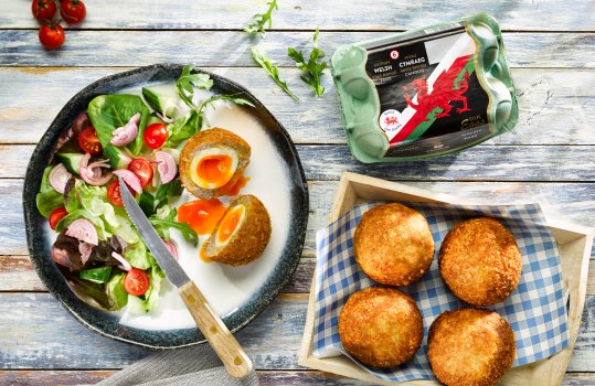 Food photograph of a tray of homemade scotch eggs, with one scotch egg cut in half to expose the runny yolk, plated up with a side salad.