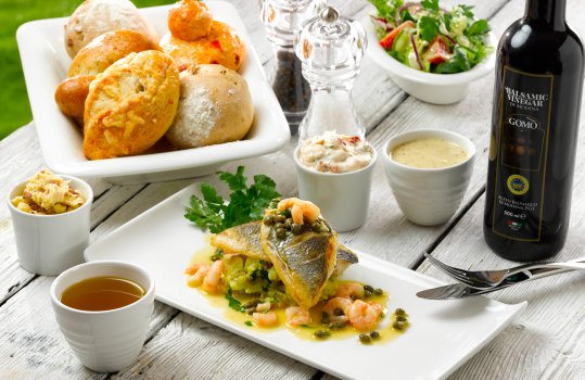 Food photograph of al fresco dining including pan fried fish with brown shrimp and capers, alongside a bowl of bread and a side salad